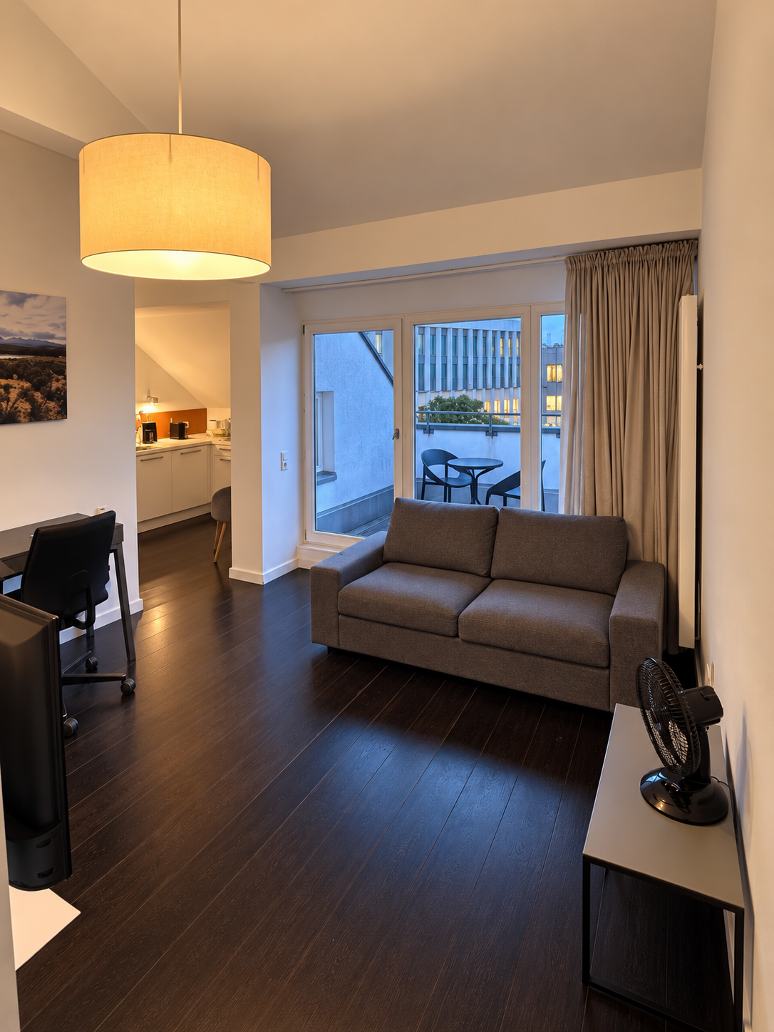 Dachgeschoss-Apartment: Wohnbereich mit Sofa und Stehlampe, Blick zur Küchenzeile und zum Ausgang