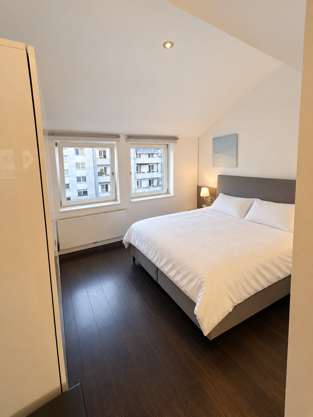 Dachgeschoss-Apartment: Schlafzimmer mit Doppelbett und zwei Fenstern unter der Dachschräge